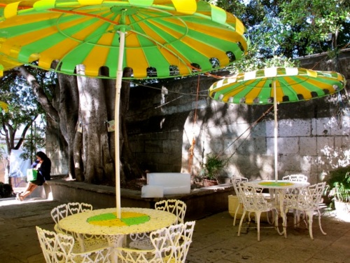 Green and yellow iron chairs and umbrellas in front of a neveria stand.